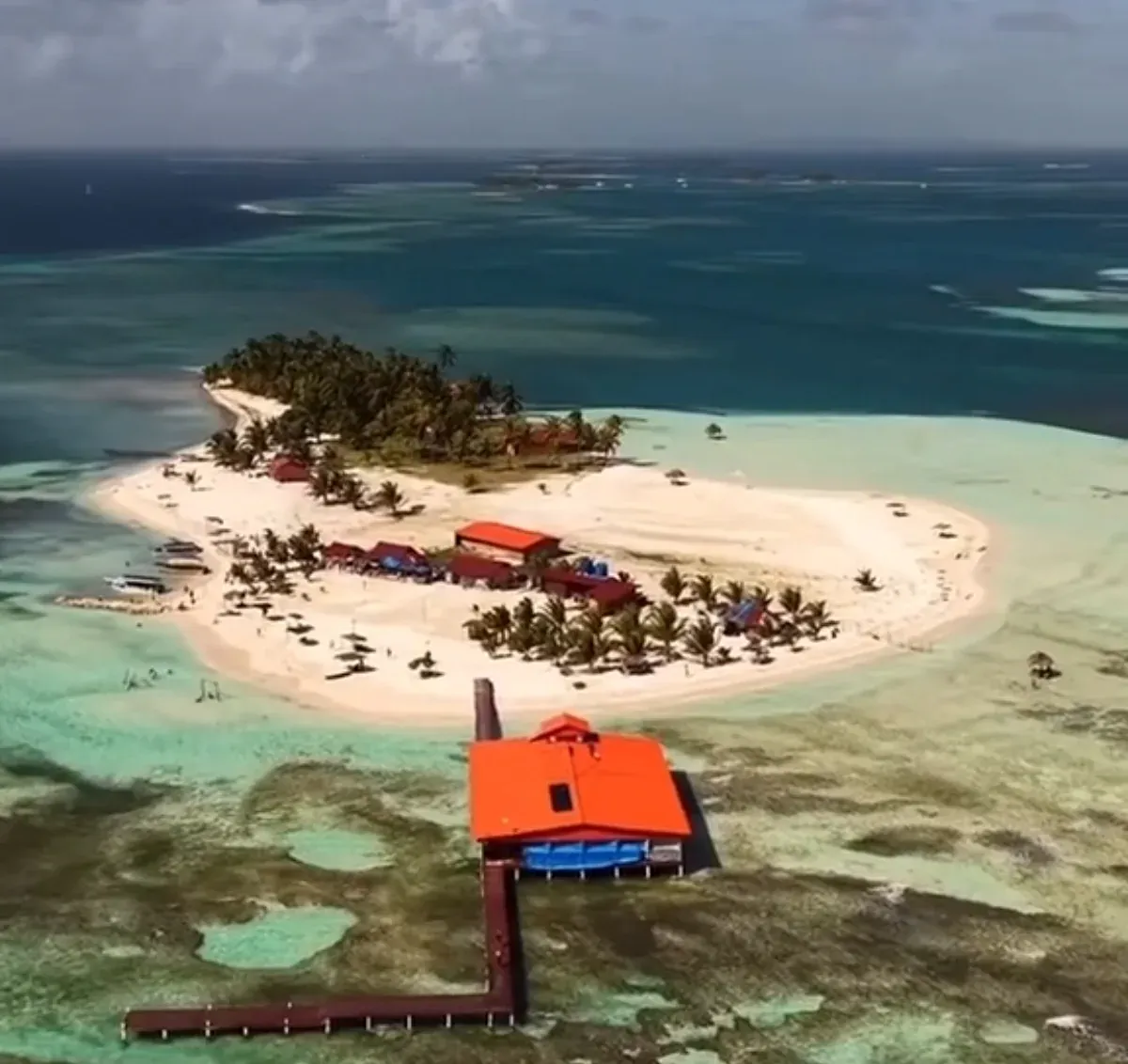 Vista aérea de la isla en Guna Yala: arena blanca, palmeras y el muelle con techo naranja sobre el agua turquesa